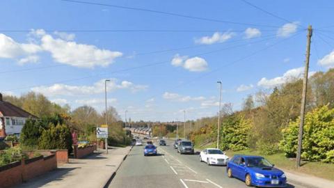 A Google street view of Violet Hill, in Mansfield, with houses on the left and trees on the right. Cars are driving on the road 