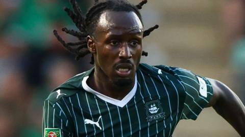 Malachi Boateng wearing the green and white pin striped strip of Plymouth Argyle. He has long dreadlocked hair.