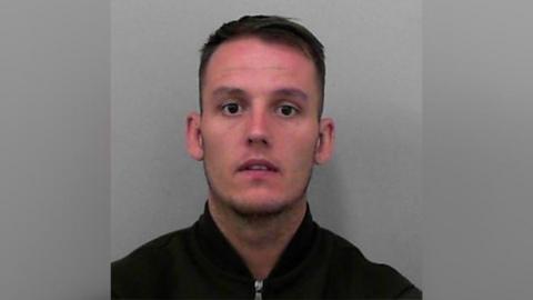 A police custody photo of Joe Hatherall. He has short dark-brown hair and is wearing a black zip-up jacket.