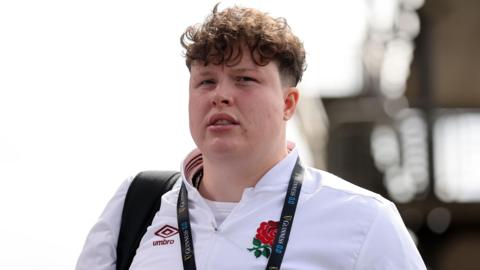 England rugby player Hannah Botterman wearing a white England tracksuit top with a black rucksack over her shoulder walking into Twickenham