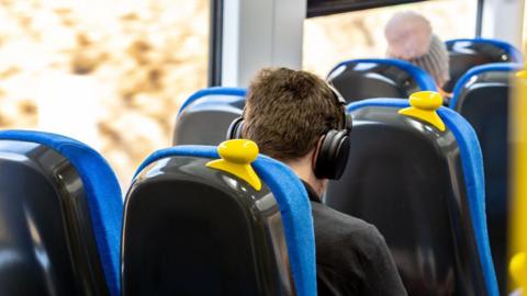 A photo taken from behind of a man sitting on a train with headphones on. 