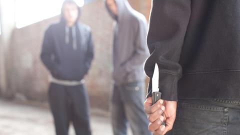 A stock photo of two men being confronted by man with knife. All people in the photo are anonymous.