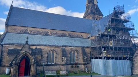 St James Church building with scaffolding covering the right side with workmen on wooden platforms. 