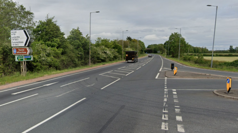 A general view of the A75 near Annan. The sky is grey. The road is tarmac and has patches of green on either side.