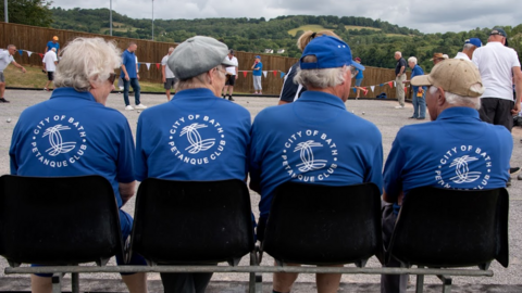 Rear view of four members of the club, with branded t-shirts, sitting watching members on the pistes