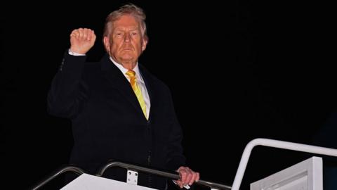 Donald Trump stands as he boards Air Force One, with one fist in the air, the other hand holding on to the rail