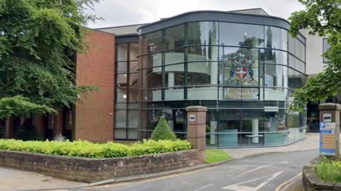 A glass fronted building set behind a sandstone wall entrance. A stained glass panel features the writing Liverpool Hope University along with the university crest.