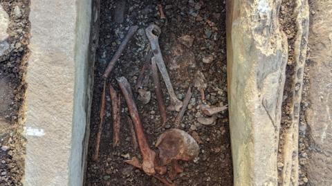 A burial cist, with bones visible - they are in the process of being excavated