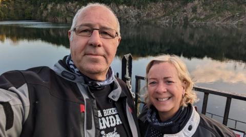 A man and a woman standing in front of a lake. 