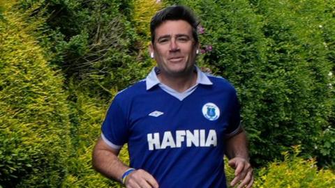 Andy Burnham, who has dark hair, photographed while running. He is wearing a retro blue Everton FC shirt from the 1980s.
