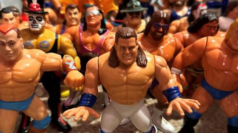 A collection figures of various wrestlers all standing in a huddle. They are bulky and muscly figures, rather cartoon like.
