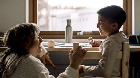 Smiling boy talking with a woman while sitting on chair at home.