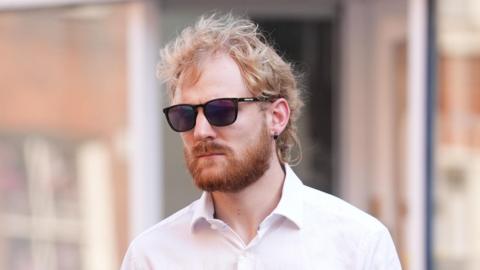 A image of a man with blond hair and an earring wearing sunglasses. 