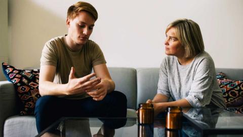 A man and woman sit on the sofa looking serious.