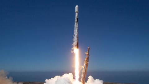 A satellite being launched into the space by a Space X rocket on a blue clear day.