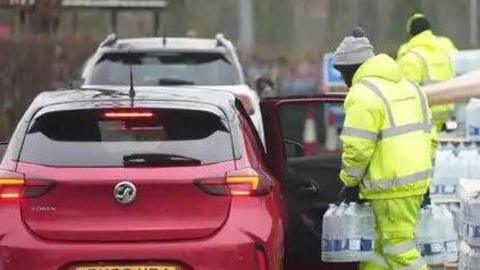 Workmen in hi-vis jackets passing water bottles into the back of a red car at a water bottle station