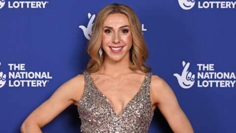 Picture of Lauren Drew at the National Lottery's Big Night of Musicals Red Carpet at the AO Arena. She is smiling at the camera wearing a sparkly silver dress with curly light brown hair. 