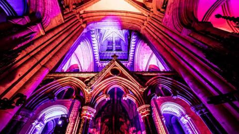 An interior section of Durham Cathedral lit up red and purple on Tuesday 7 October 2025.