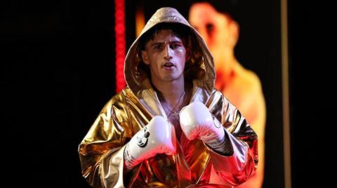 Royston Barney-Smith makes his way to the ring, dressed in a gold gown and wearing white boxing gloves