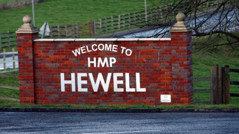 A red brick sign reading "welcome to HMP Hewell". 