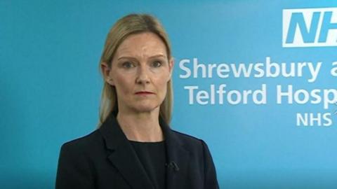 Louise Barnett standing in front of a blue background with NHS branding