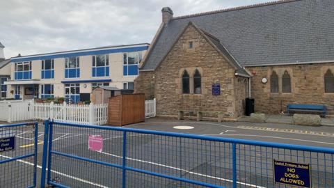 Castel Primary School with a blue fence in front of a playground with the school buildings behind