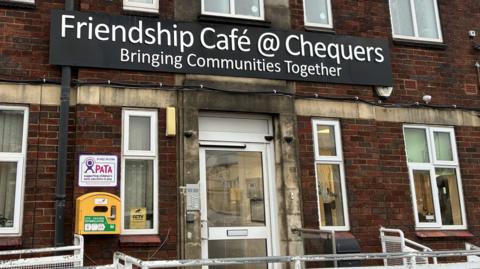 A photo of the outside of a building which a large sign which reads Friendship Cafe @ Chequers