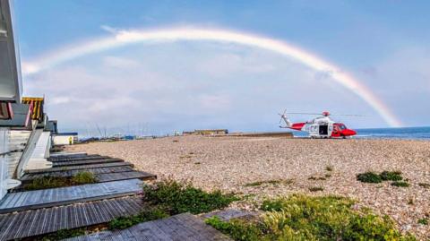 Coastguard helicopter landed on a beach with beach huts to the left and the sea to the right.