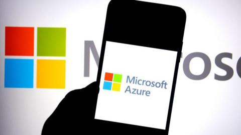 A silhouetted hand holding a phone with the words "Microsoft Azure" on it. In the background is the red, green, blue and yellow Microsoft logo.