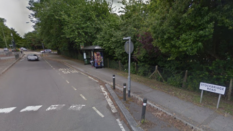 Road with crossing and bus stop on the right with cars travelling in the distance.