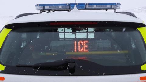 Back of a police car displaying the message 'ice' on a snowy day.