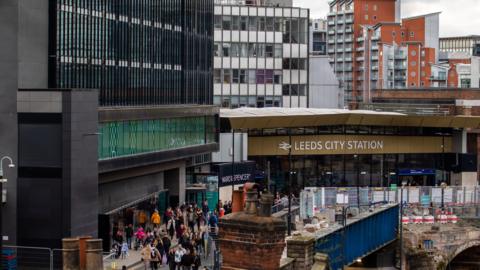 General view of Leeds City Station, with passengers walking in front of the entrance.
