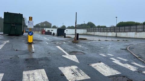 The former Ford Hill tip in Queensbury, with a refuse container standing in the background and road markings indicating the direction of travel through the site.