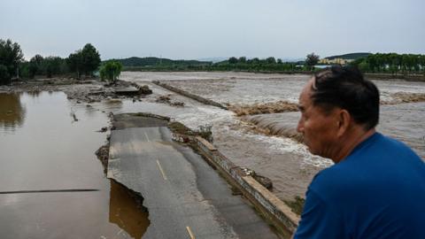 Man looks at a flooded and damaged road in Beijing, China