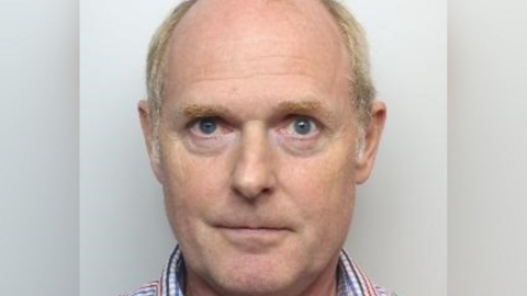 A custody picture of an older man with thinning hair who wears a checked shirt.