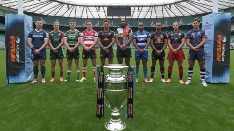 A player from each of the 10 Prem clubs stands beneath the posts at Twickenham on the pitch with the Prem trophy on the floor in front of them