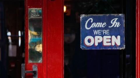 A red pub door with a 'Come in we're open' sign