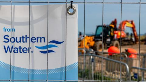 Security fencing and public information posters near the preparations for the laying of a new outfall pipe from at Swalecliffe wastewater treatment works, operated by Southern Water Ltd