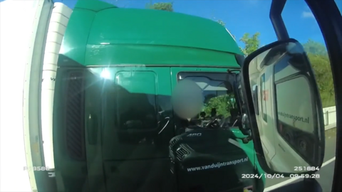 A green HGV with a driver, whose face has been blurred, sitting behind the wheel