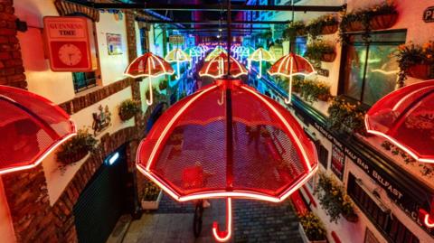 Different coloured umbrellas hanging on lines above a street.