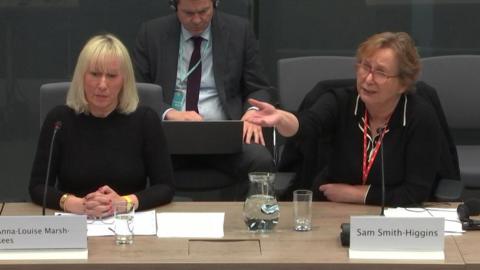 Two members of the bereaved families group with their names Anna-Louise Marsh-Rees and Sam Smith-Higgins written on cards in front of them. Ms Marsh-Rees, who is sat tot he left, is staring ahead of her, while Ms Smith-Higgins is gesturing to her right and looks concerned.