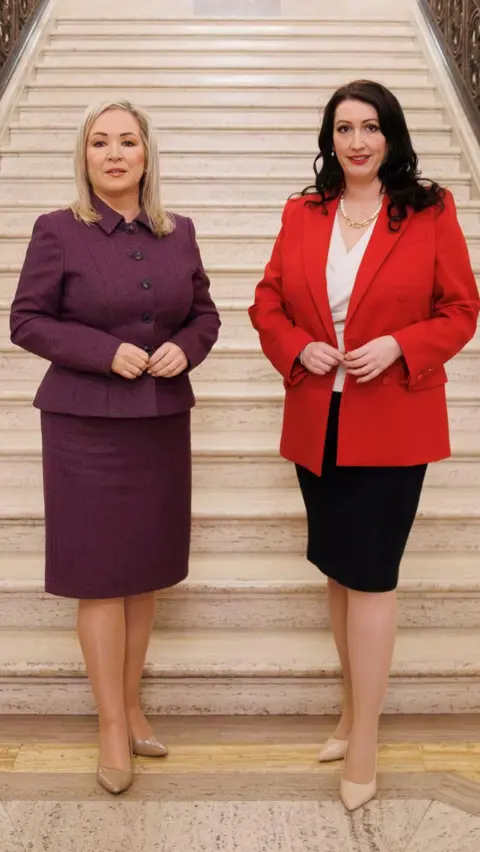 Michelle O'Neill and Emma Little-Pengelly stand at the bottom of a white marble staircase in Stormont.