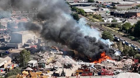 Drone shot of flames and smoke coming from an industrial yard.
