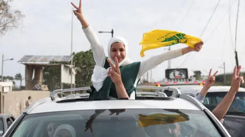 eople show victory signs from a vehicle as displaced people cross the bridge linking southern Lebanon