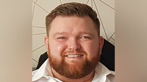 Man with a ginger beard smiling at the camera. He is wearing a white shirt.