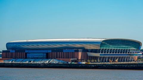 Image shows the Hill Dickinson Stadium, home to Everton FC. It is an oval-shaped stadium that sits on the Liverpool waterfront to the north of the city. 