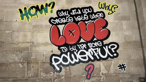 "Why did you create hate when love is more powerful?" written in graffiti font on wall of Canterbury Cathedral crypt