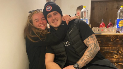 MMA fighter Brett Nolan with his friend Nicole Ingall. The two are sitting close together, Nicole has her arms around Brett's shoulders. Both are wearing dark coloured clothes and smiling.