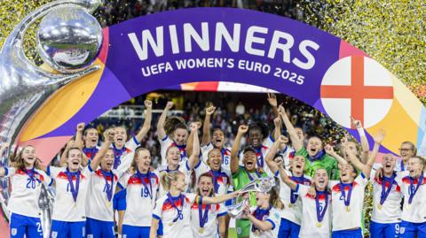 the england team celebrating on the podium in the stadium where they played against spain with confetti flying