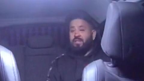 A man sitting in the back of a police car in a black hoodie. He has a black beard and short black hair